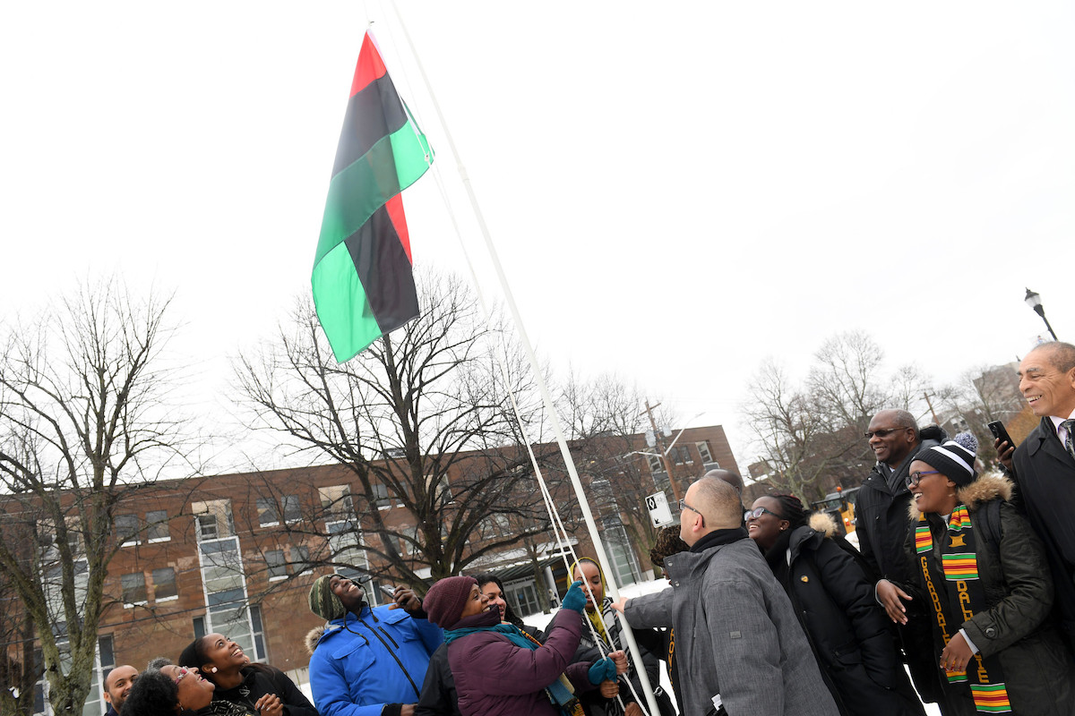 Group of people in outdoors in winter gathered around pole flying the Pan-African flac.