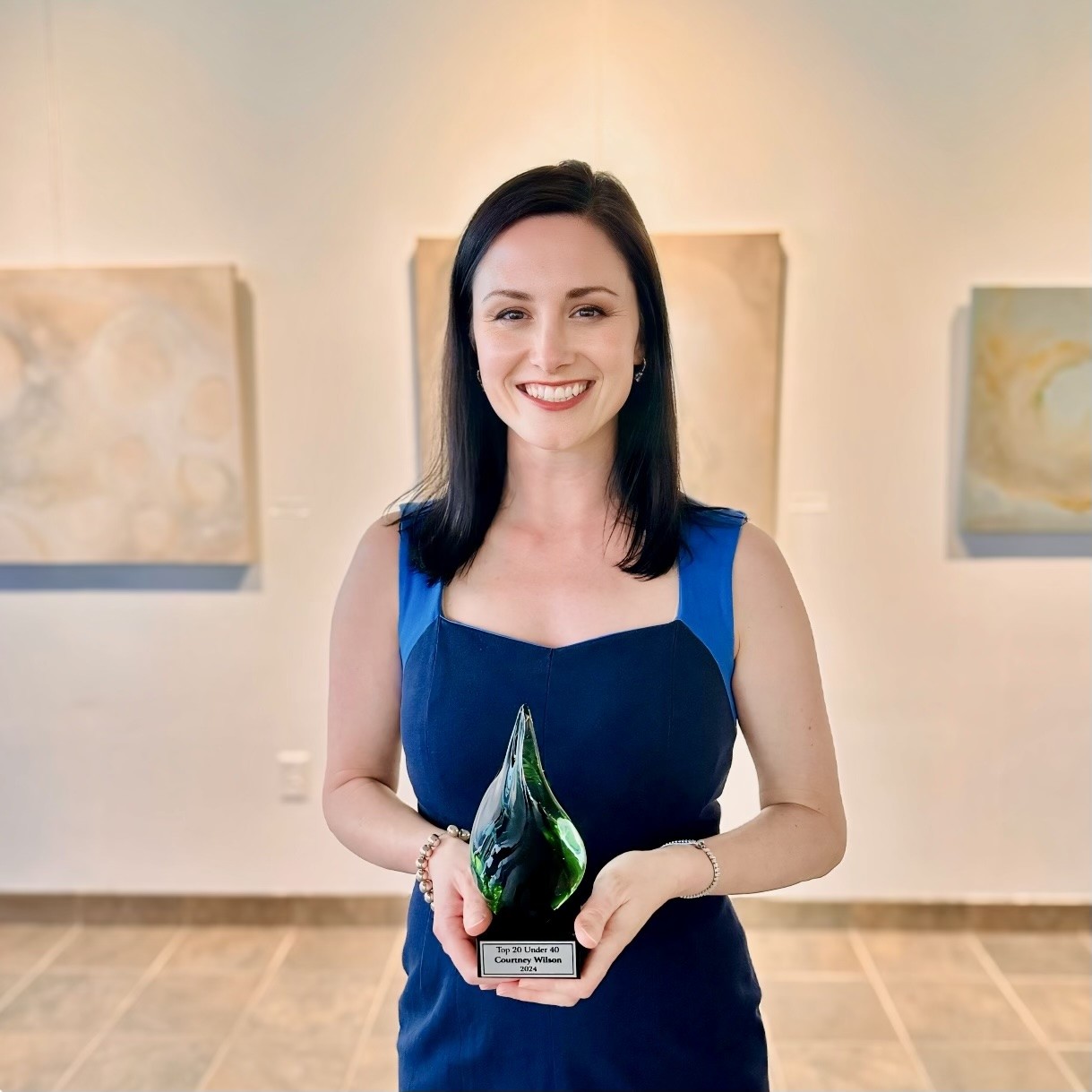 Wilson holds an award standing in front of artwork on the walls at an event .