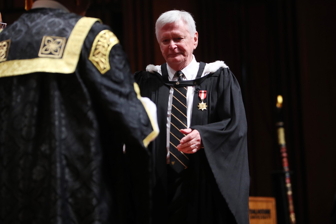 Clark wearing a graduation gown and crossing the stage to accept his degree.