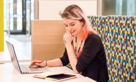 Student sitting at a table with a computer and a book