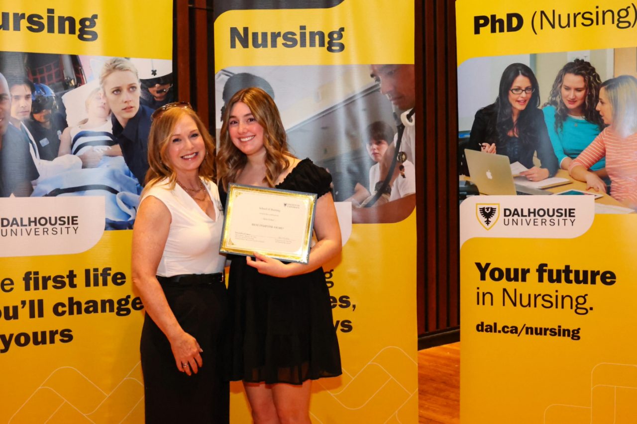 Two women, one who is holding a certificate, pose in front of three yellow banners
