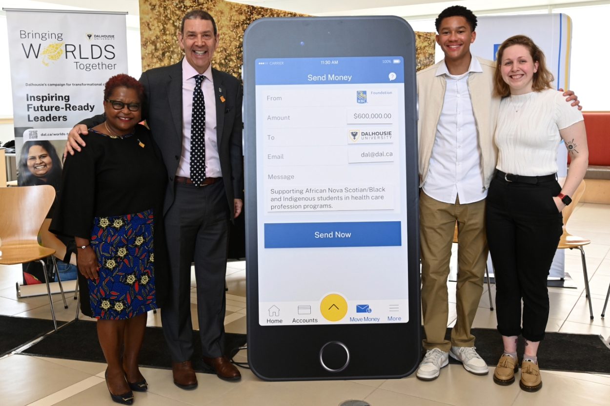 A group of four people stand around a large cut out of a cell phone