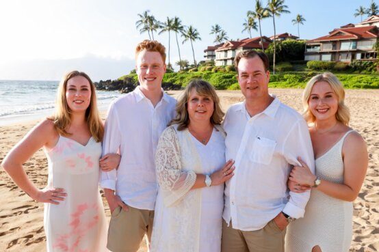 A family of five poses together in formal wear on the beach with villas in the background.